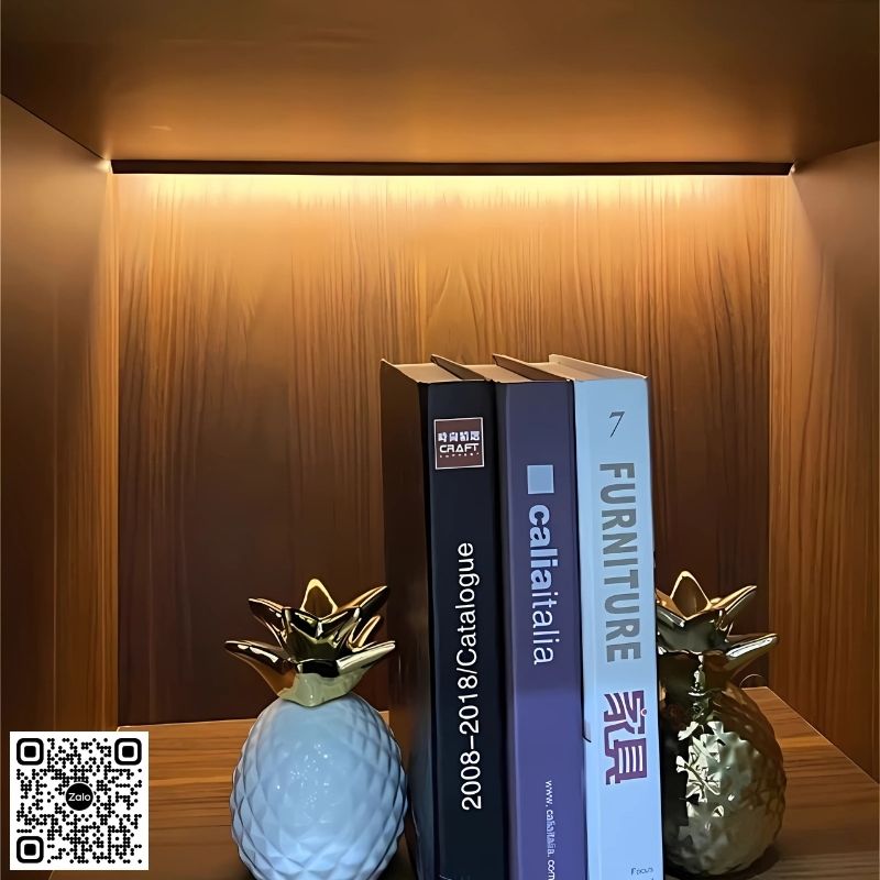 14-15 Sách catalogue nội thất đặt trên kệ gỗ có đèn LED, trang trí cùng tượng quả dứa sứ mạ vàng